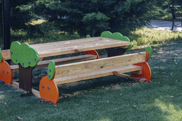 A vibrant wooden picnic table with colorful tree designs stands in a green park, surrounded by