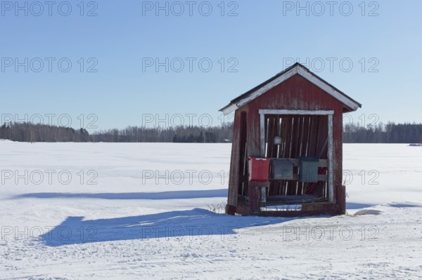 Old weathered red hut with three mail boxes by rural road in winter with snow covering the ground,
