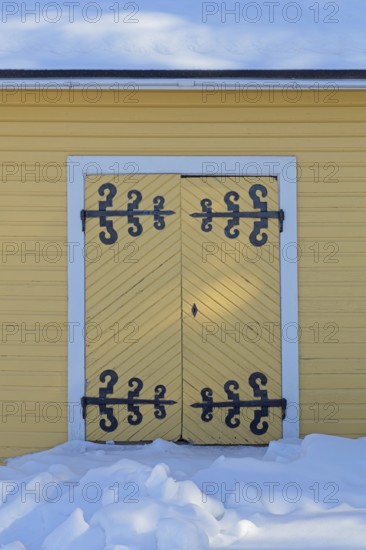 Old wooden double doors with wrought iron decorative hinges in winter with snow on the ground,