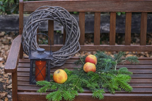 Wooden bench with apples, pine branches, wreath and lantern in rustic style, North