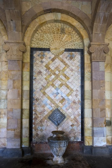 Detailed mosaic with decorative patterns and reliefs on the wall above a stone jug, spring, mineral