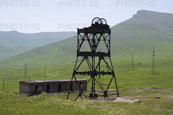 An abandoned structure in a green mountain landscape with ruined buildings and power poles, disused