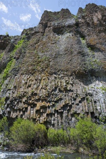 Basalt columns and lush greenery form an impressive cliff landscape on the river under a blue sky,