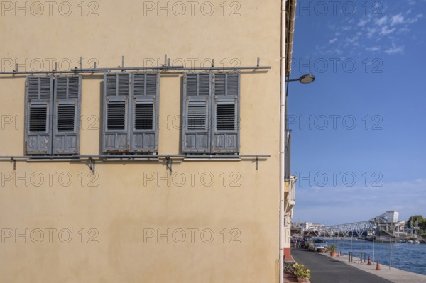 Yellow house façade with three gray wooden shutters to move and a view across the Canal de Sete