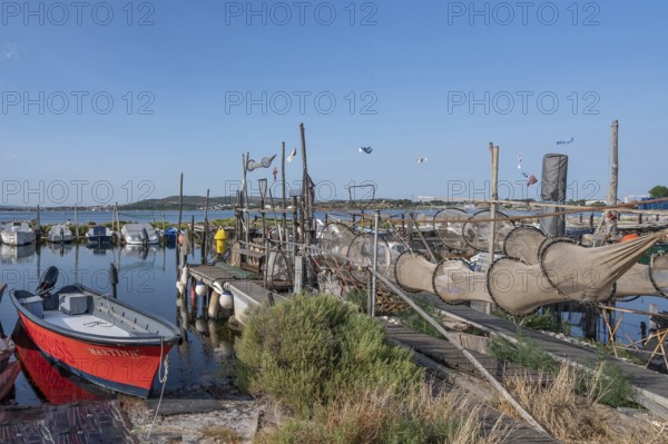 A red fishing boat is lying in the foreground on a wooden pier where numerous fish traps and nets
