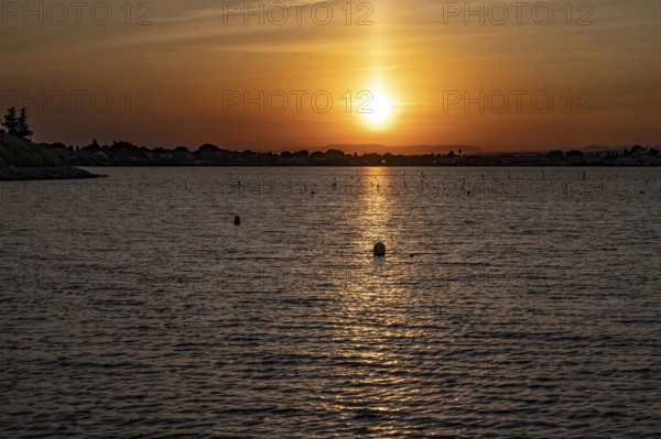 A golden sunset over the Etang de Thau with strong light reflection on the water surface, the