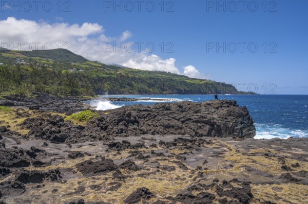 An angler stands on a massive rock of the black lava coast and looks out at the roaring Indian