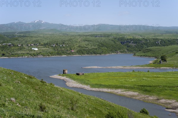 Winding river flows into a lake surrounded by green hills under a blue sky, Kechut Reservoir,