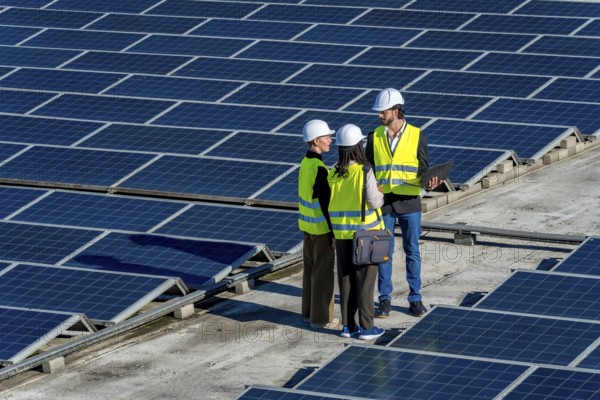 Group of diverse engineers in hard hats and vests working on a solar power station, discussing
