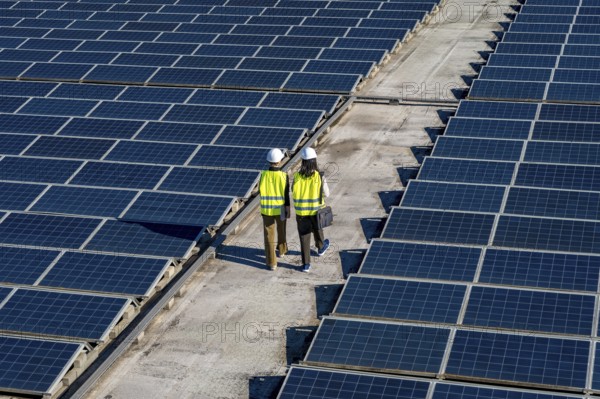 Two engineers, wearing hard hats and safety vests, walking between rows of solar panels on a
