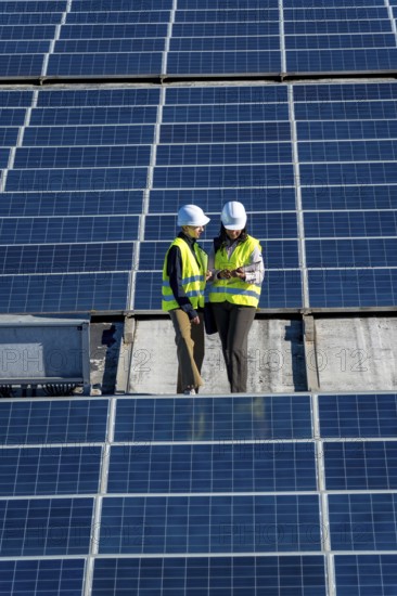 Female engineers wearing hard hats and high visibility vests discussing data on a digital tablet