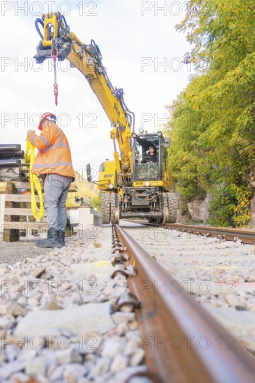 Excavator working on track, construction worker checking equipment, focus on rails, autumn