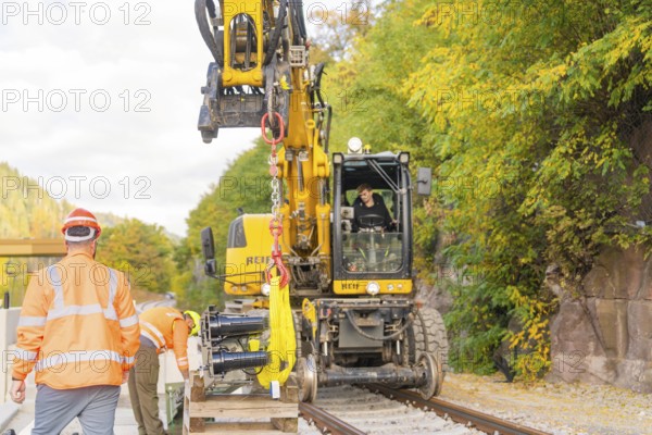 Excavator lifts objects on train tracks, construction workers talking, autumn environment, signal