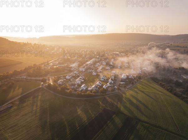 A village surrounded by fields in fog at sunrise with warm orange light, Calw Stammheim, Black