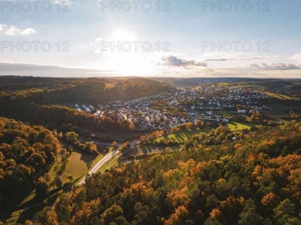Colourful autumn landscape with a view of a village and vast forests under the evening sun,