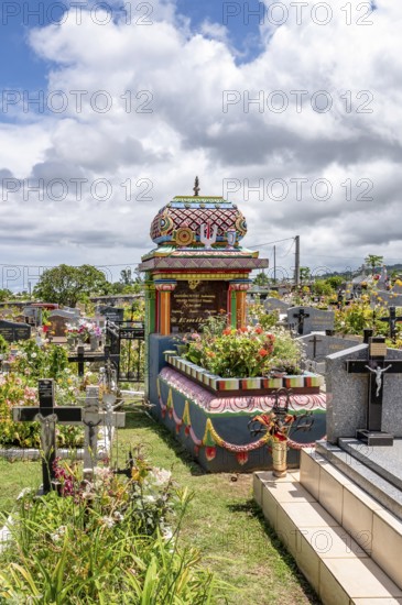 A colorful, richly decorated Hindu shrine with a small temple roof in the cemetery stands between