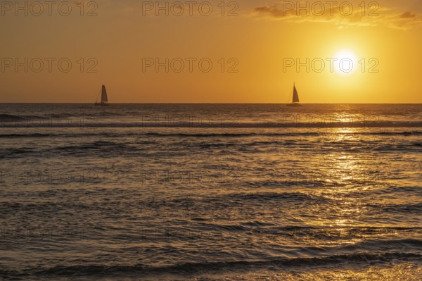 A warm sunset light bathes the sky over the Indian Ocean in orange and gold as two small sailboats
