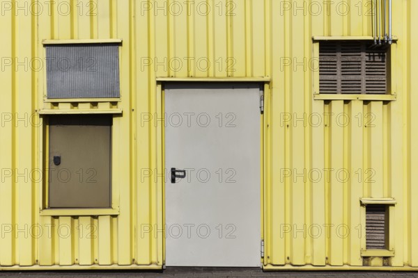 Yellow profiled sheet façade of an industrial building, doors and openings with ventilation