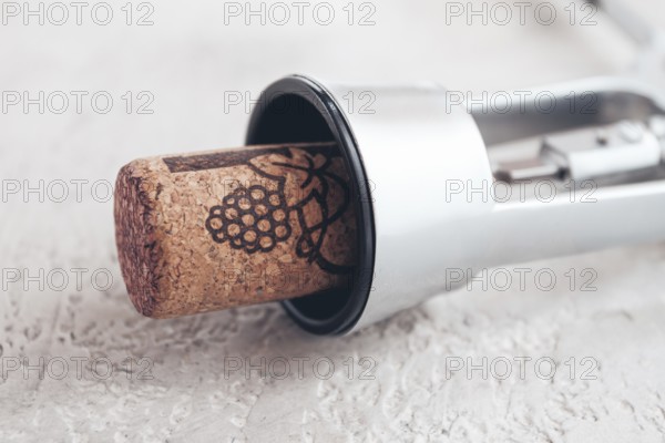 A shiny silver corkscrew rests on a light textured surface, with a wine cork partially inserted,