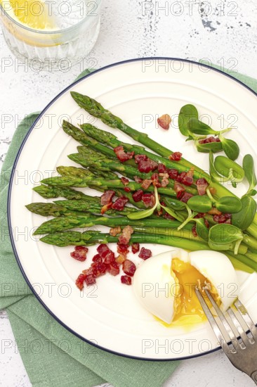 Poached egg with fork, asparagus, bacon slices and herbs, on a white plate, breakfast, close-up, no
