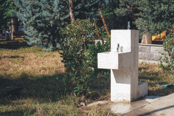 In a peaceful park, a modern water fountain is positioned among lush green plants and grass. The
