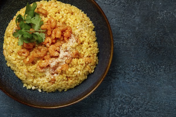 Risotto with shrimp, in a bowl, on a textured surface, with a side dish of fresh coriander,