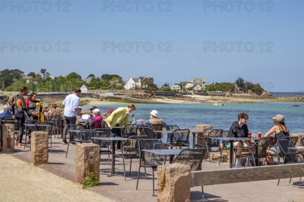 Numerous guests sit at small tables on the sunny terrace of the Grand Hotel Du Port Blanc on the