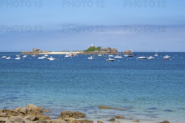 In the turquoise-blue waters of the English Channel, motor boats and sailboats anchor off small,