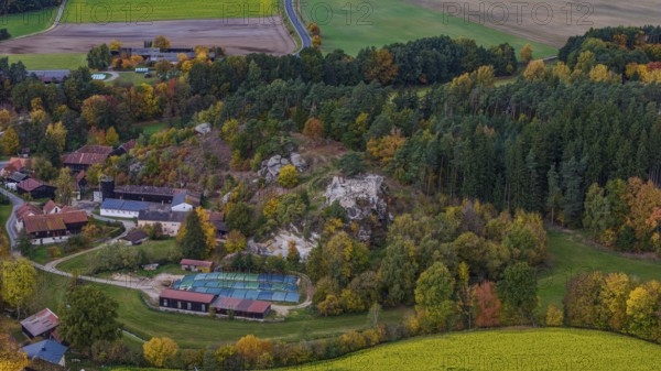 A picturesque village is surrounded by colorful trees in autumn. A castle ruin is nearby, while the