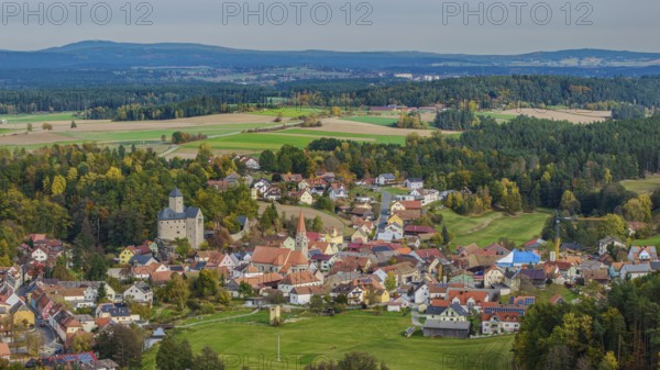A gentle hilly landscape surrounds a small village with colorful houses and an old castle. The