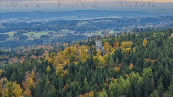 The ruins of Weissenstein Castle rise above a colorful forest whose leaves glow in autumn. The