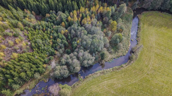The river snakes through the countryside, surrounded by green trees and golden yellow leaves. The