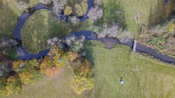 The scene shows a quiet river flowing through a picturesque meadow. Autumn colors of the trees and