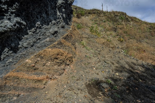The scene shows different layers of earth and rock formations in a rural area on a clear day. Dry