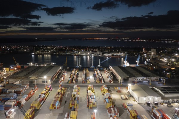 Night view of a bustling port with illuminated containers and cranes by the waterfront. Aerial view