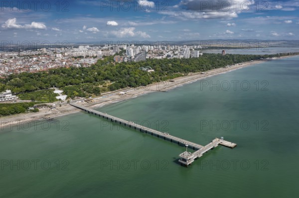 Aerial view of a long pier extending into the sea with cityscape in the background. Aerial view to