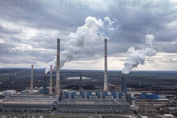Aerial view of a large power plant with smokestacks emitting smoke into a cloudy sky. Aerial view