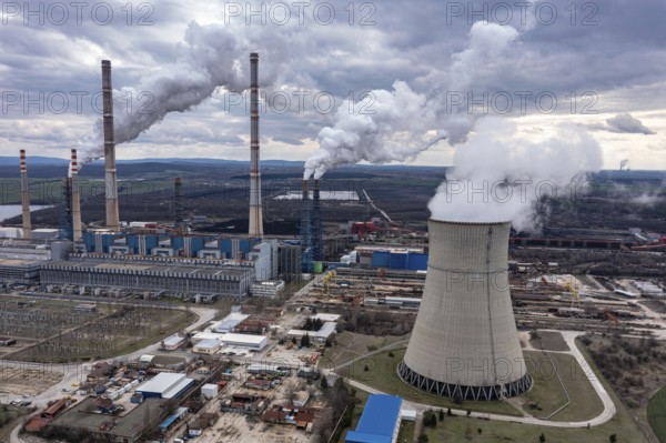 Aerial view of a power plant with multiple smokestacks releasing smoke under a cloudy sky. Aerial