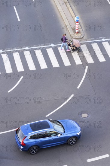 Blue car heading to pedestrian crossing with unrecognizable young woman pushing baby carriage,