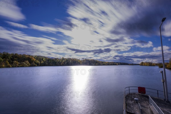 A quiet river stretches under a cloudy sky. The clouds move gently while the sunlight makes the