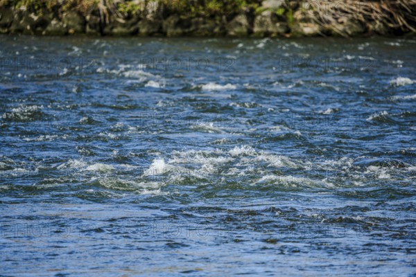 The clear water surface of a river shows soft waves that are created by the movement of the water.