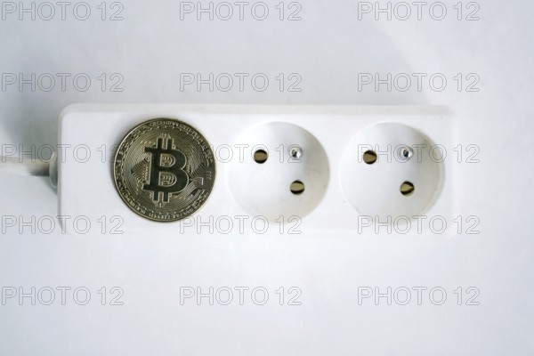 Bitcoin coin lying on power strip extension cord with two empty sockets, cryptocurrency investing,