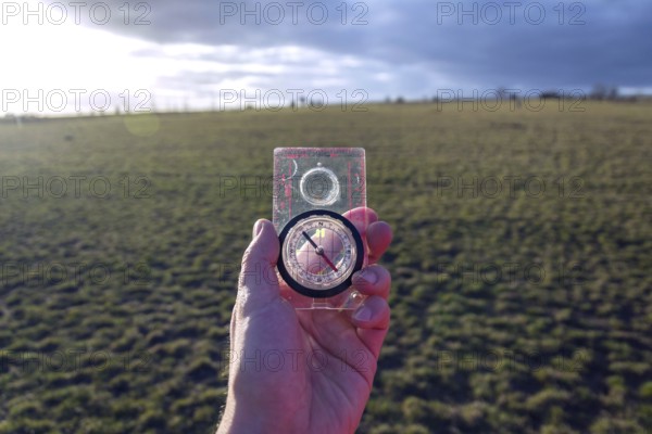 Male hand holding glass compass, nature in background, sunny autumn day, life change and new years