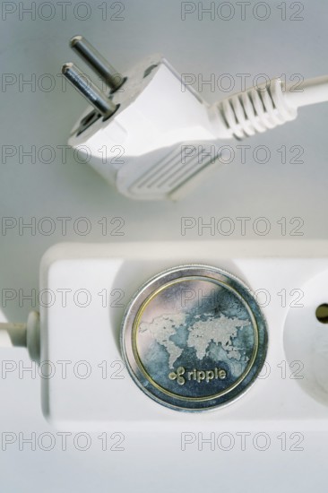 Ripple coin lying on power strip extension cord with empty socket, cryptocurrency investing, energy