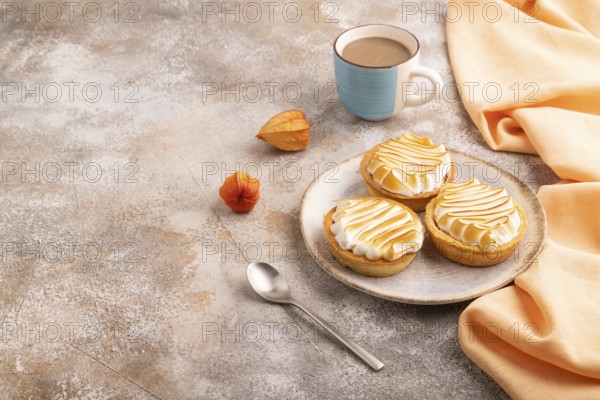 French lemon tart with meringue on brown concrete background, cup of coffee, orange linen textile,