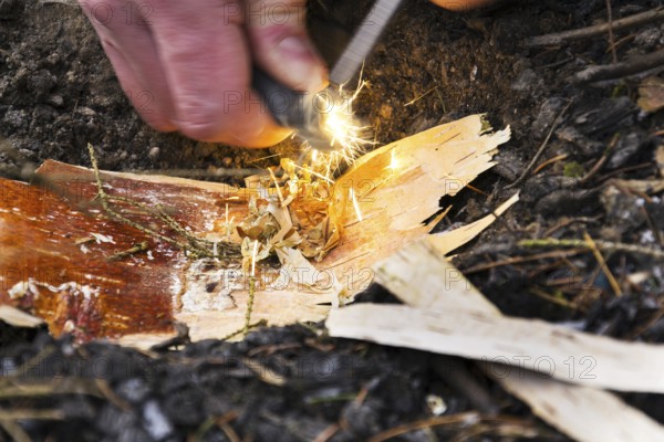 Male hand starts fire with magnesium fire steel, fire striker
