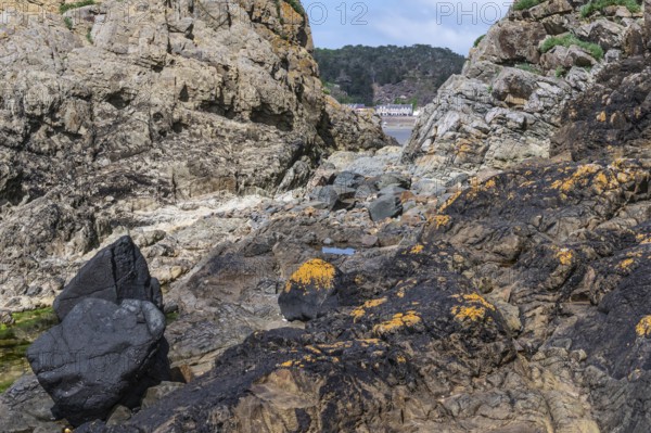 A rugged rock formation, dark and yellow-orange covered with lichens, which forms a narrow opening