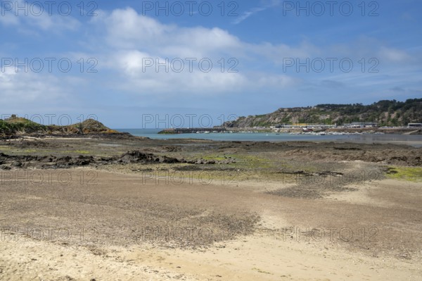 An extensive, humid sandy and rocky beach at low tide stretches out in the foreground, while in the