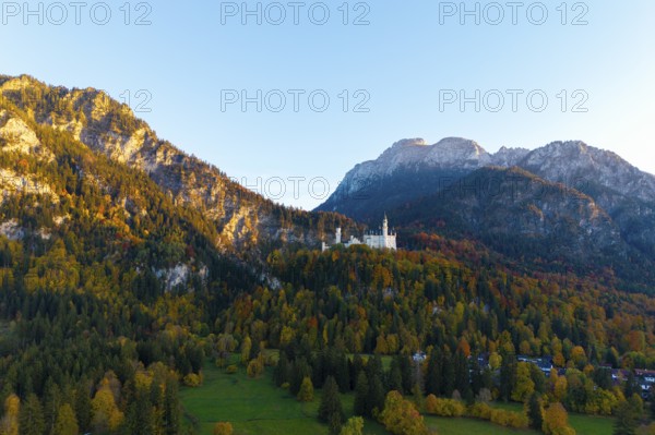 Neuschwanstein Castle perched on a wooded mountain in autumn light with a wide view of the valley,