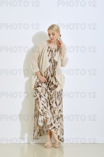 A woman showcases a fashionable long dress with a unique pattern. She stands elegantly by a wall,